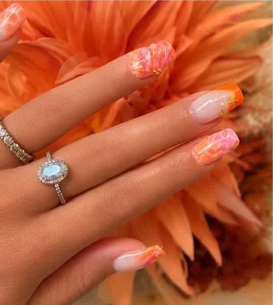 Détail d’ongles effet aquarelle corail avec étoiles dorées